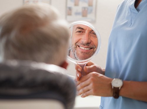 Man smiling at reflection in handheld mirror