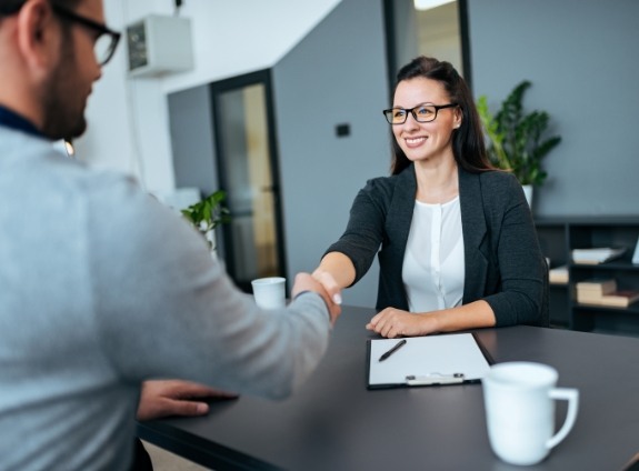 Two people shaking hands from across desk