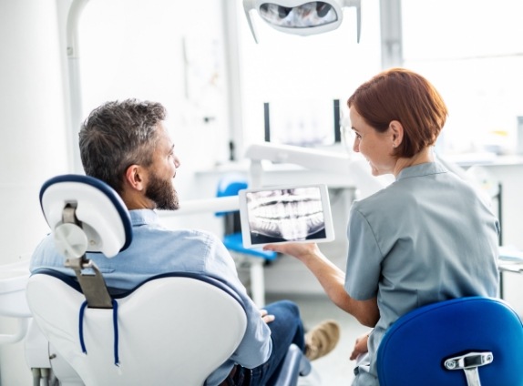 Man in dental chair talking to dental team member