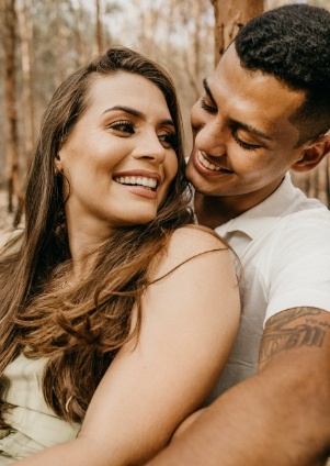 Smiling man hugging woman from behind in forest