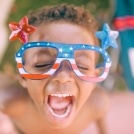 Grinning child wearing red white and blue sunglasses outdoors