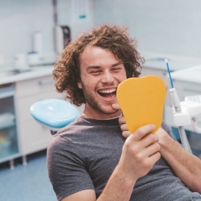 Young man in dental chair looking at his smile in mirror