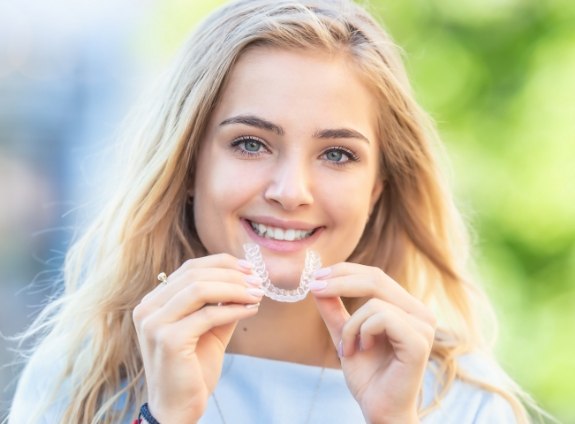 Smiling blonde woman holding Invisalign clear aligner in Santa Clarita