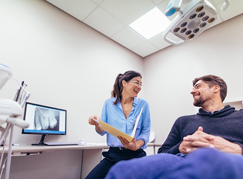 Dentist and patient smiling while reviewing X-ray in office