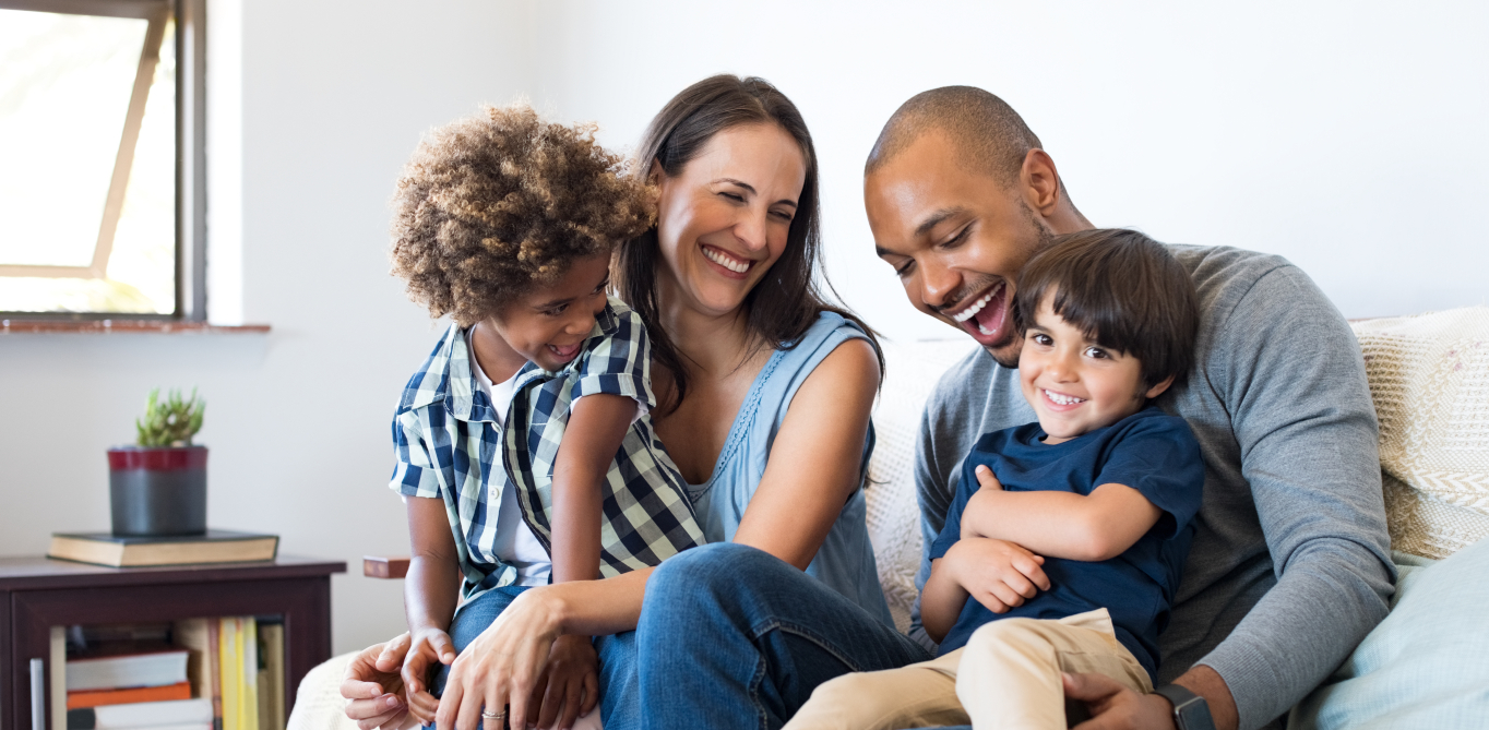 Family of four smiling on couch after receiving dental services in Santa Clarita